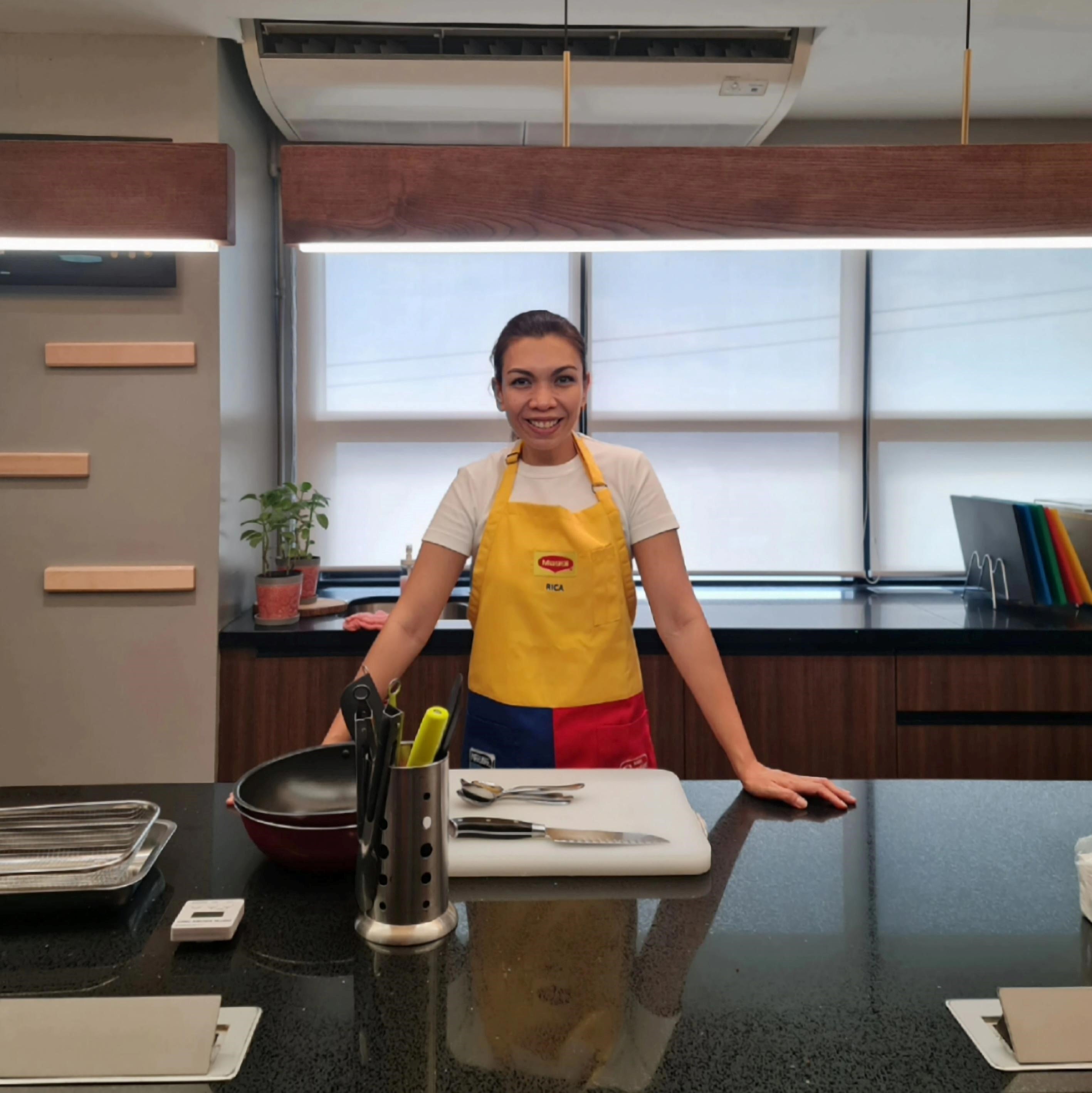 A person in a yellow &quot;Maggi&quot; apron stands at a modern kitchen counter.